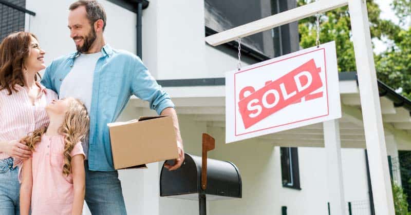 Family standing in front of a home with a "Sold" sign